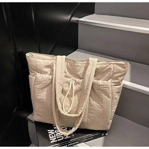 Detail of beige quilted nylon tote bag featuring drawstring pockets on a minimalist staircase