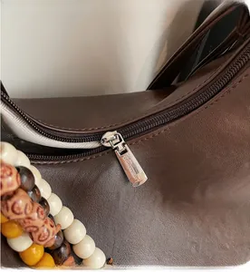 Detail of smooth metal zipper and colorful beaded pendant on brown leather hobo bag