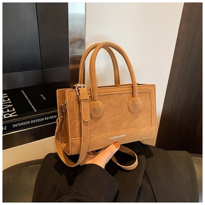 Close-up of tan matte leather handbag with cylindrical dual handles and long strap