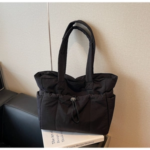 Detail view of black padded tote bag with adjustable drawstrings and side pockets on sofa
