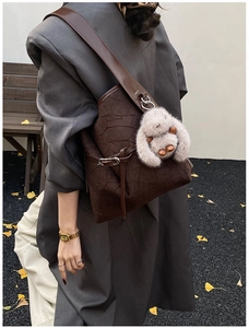 Detail of dark brown pleated hobo bag with plush rabbit charm and wide shoulder strap