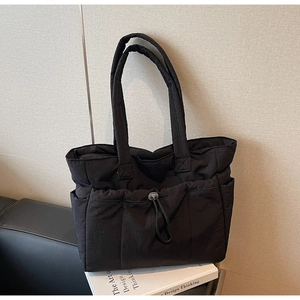 Detail of black quilted tote bag with drawstring closure on a leather sofa with a book