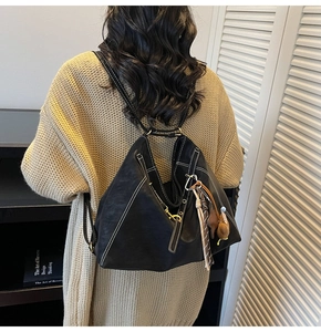 Detail of a black geometric backpack with white contrast stitching and decorative pendants