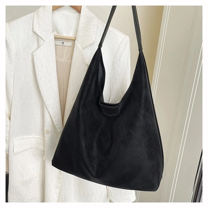 Detail shot of black minimalist suede tote bag hanging next to a white textured blazer