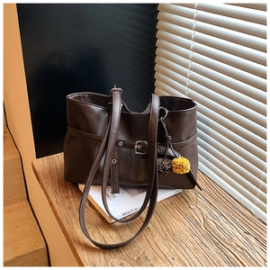 Close-up of a large dark brown leather tote bag featuring decorative wrap-around buckle straps