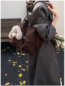 Macro detail of dark brown pleated leather tote bag featuring a cute bunny plush charm