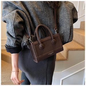 Detail of dark brown faux leather handbag showing round metal buckles and brand logo