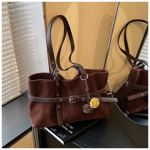 Detail of dark brown suede tote bag featuring decorative belt and floral ball charms