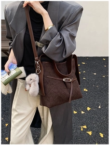 Detail of a dark brown textured tote bag with a plush rabbit charm on a stylish model