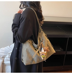 Detail view of large olive green tote bag with white stitching and plush charms on shoulder