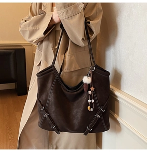 Détail d'un grand sac cabas marron foncé avec coutures blanches et accessoire décoratif