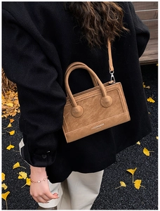 Detail of tan suede crossbody bag with brand logo styled on a tweed coat outdoors