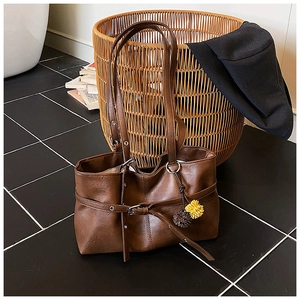 Close-up of vintage brown leather tote bag with decorative metal buckle and pompom charm