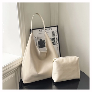 Detail view of cream minimalist leather tote bag and matching pouch on a black display stand