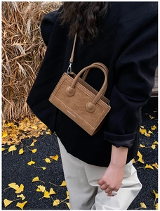 Brown suede crossbody bag with decorative round buckle shown in outdoor autumn setting