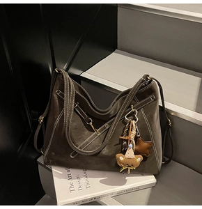 Detail of dark brown matte tote bag with contrast stitching and bear charm on stairs