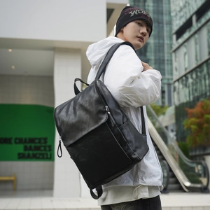 Close-up of black minimalist faux leather backpack with front flap and magnetic buckle