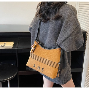 Detail view of brown suede tote bag featuring AHE embroidery and black leather strap