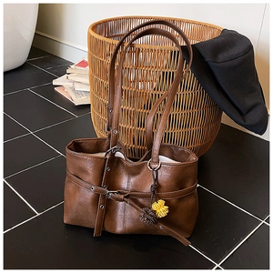 Detail of vintage brown leather tote bag with eyelet belt strap and plush pompom charm