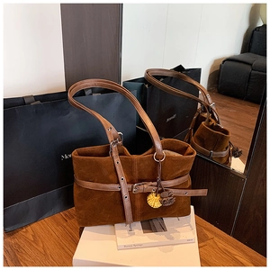 Detail view of brown suede tote bag featuring a leather buckle strap and flower charm