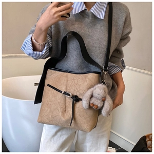 Detail of camel bucket bag with crinkled texture, black straps and plush rabbit charm