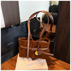 Detail of a brown suede tote bag with leather strap and fuzzy charm on wood table