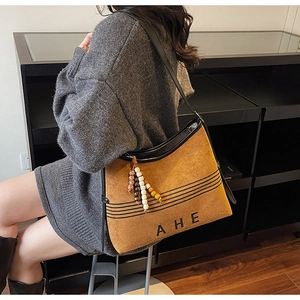 Detail of brown suede tote bag featuring black trim and vintage beaded charm accessory