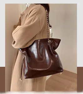 Detail of dark brown glossy leather bucket bag with chain strap and brand logo