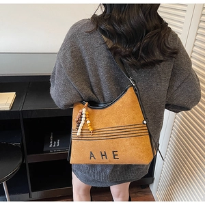 Detail of vintage brown suede hobo bag with AHE lettering and beaded charm on model