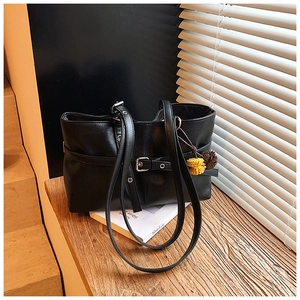 Detail of black PU leather tote bag with decorative buckle and floral charm on wooden stairs