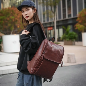 Close-up of a brown vintage faux leather backpack worn by a model in an urban outdoor setting