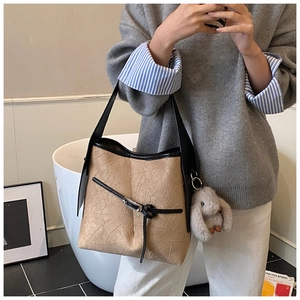 Detail of khaki pleated bucket bag with black straps and a cute rabbit charm accessory