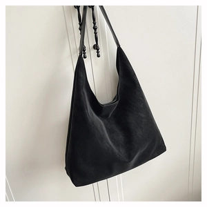 Detail of minimalist black matte leather hobo bag hanging on a door hook