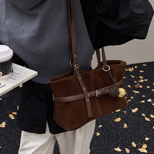 Detail of coffee brown suede tote bag with metal buckles and stylish pompom charms