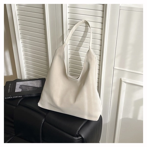 Minimalist white leather hobo tote bag shown in a lifestyle scene on a textured black sofa