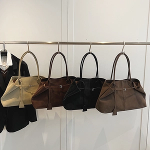 Detail of suede tote bags in beige, brown, and black with metallic buckle on a hanger