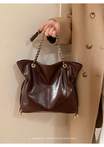 Detail of dark brown patent leather tote bag featuring chain strap and vintage texture