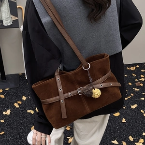 Detail of dark brown suede tote bag with buckle straps and two-tone pompom pendant