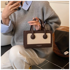 Detail view of a vintage two-tone handbag with top handles and branded logo text