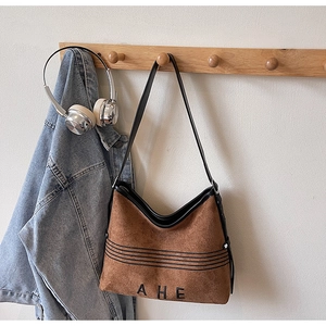 Close-up of brown suede tote bag featuring AHE logo and black stripes on a hanger