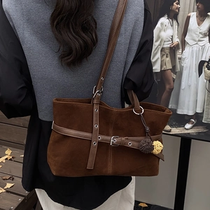 Detail of dark brown matte tote bag with decorative straps and colorful pompom charms