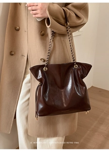Close-up of retro brown glossy leather tote bag with gold chain strap on shoulder
