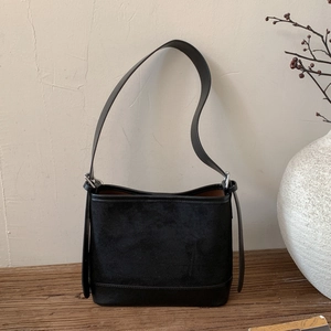 Detail of minimalist black bucket bag with mixed textures on a natural wooden surface