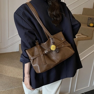 Detail of dark brown leather tote bag featuring belt buckle accents and a fur pompom charm