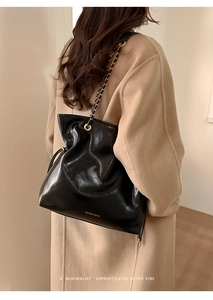 Detail of glossy black leather tote bag with gold chain strap and drawstring closure