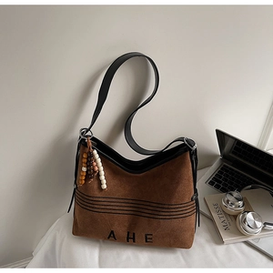 Detail of suede tote bag with AHE lettering, wooden bead charm, and laptop background