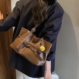 Detail of retro brown tote bag with decorative buckle and plush charms on a model