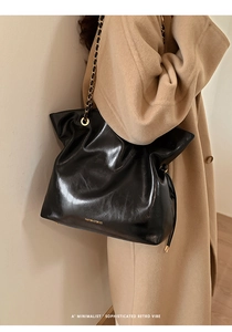 Detail of black glossy vintage tote bag with gold chain strap on camel wool coat