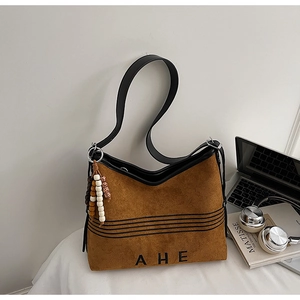 Detail of brown suede tote bag with black leather straps and wooden bead charm accessory