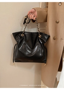 Détail de la texture en cuir noir brillant et logo doré sur le sac fourre-tout